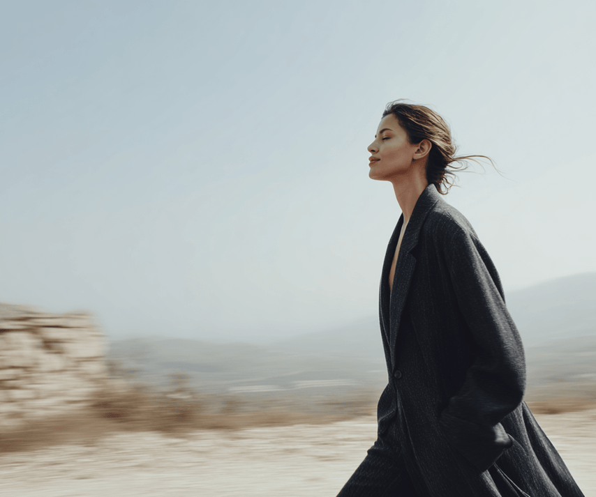 Woman in a black coat standing in a desert landscape with a blurred background