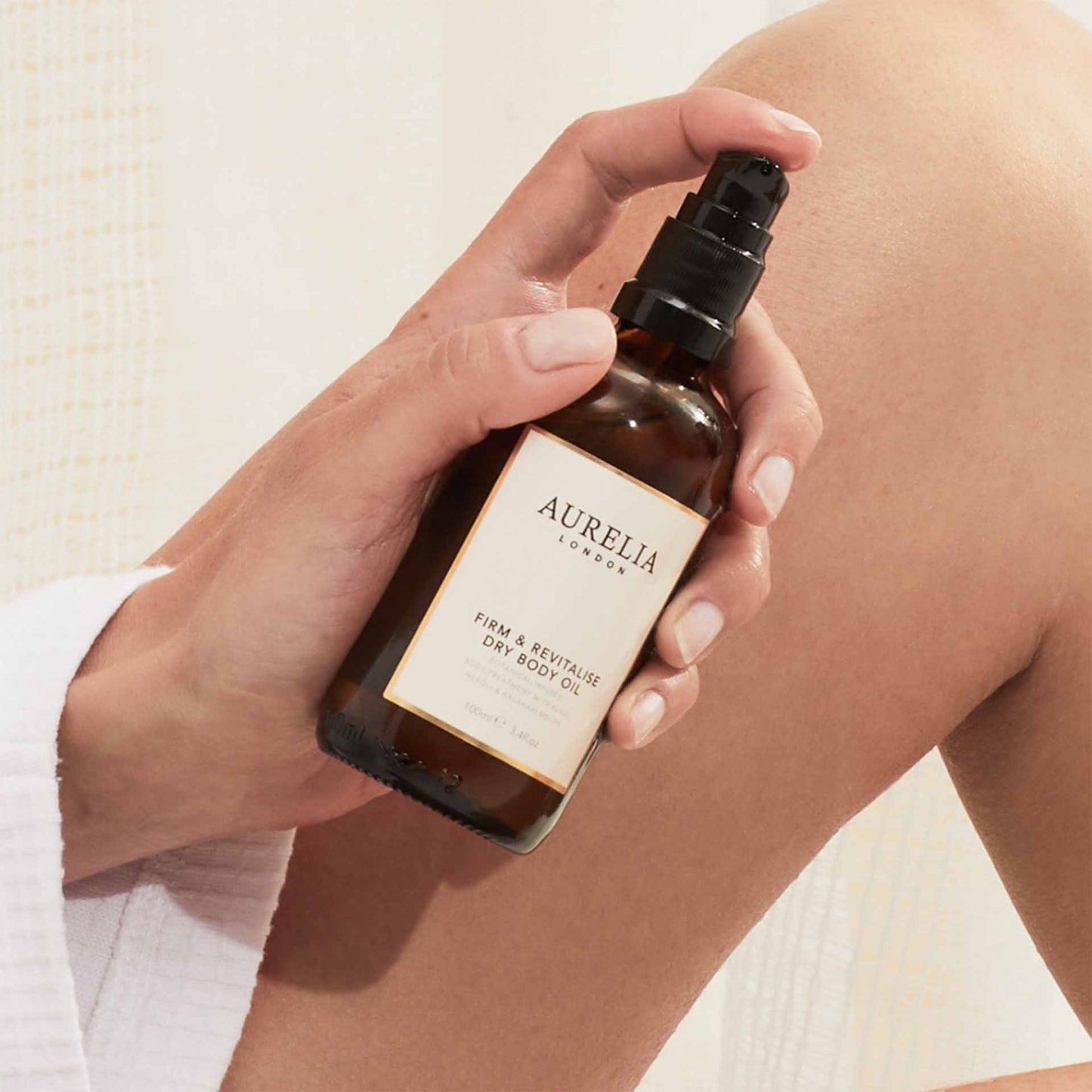 Hand holding a bottle of Aurelia London dry body oil against a neutral background