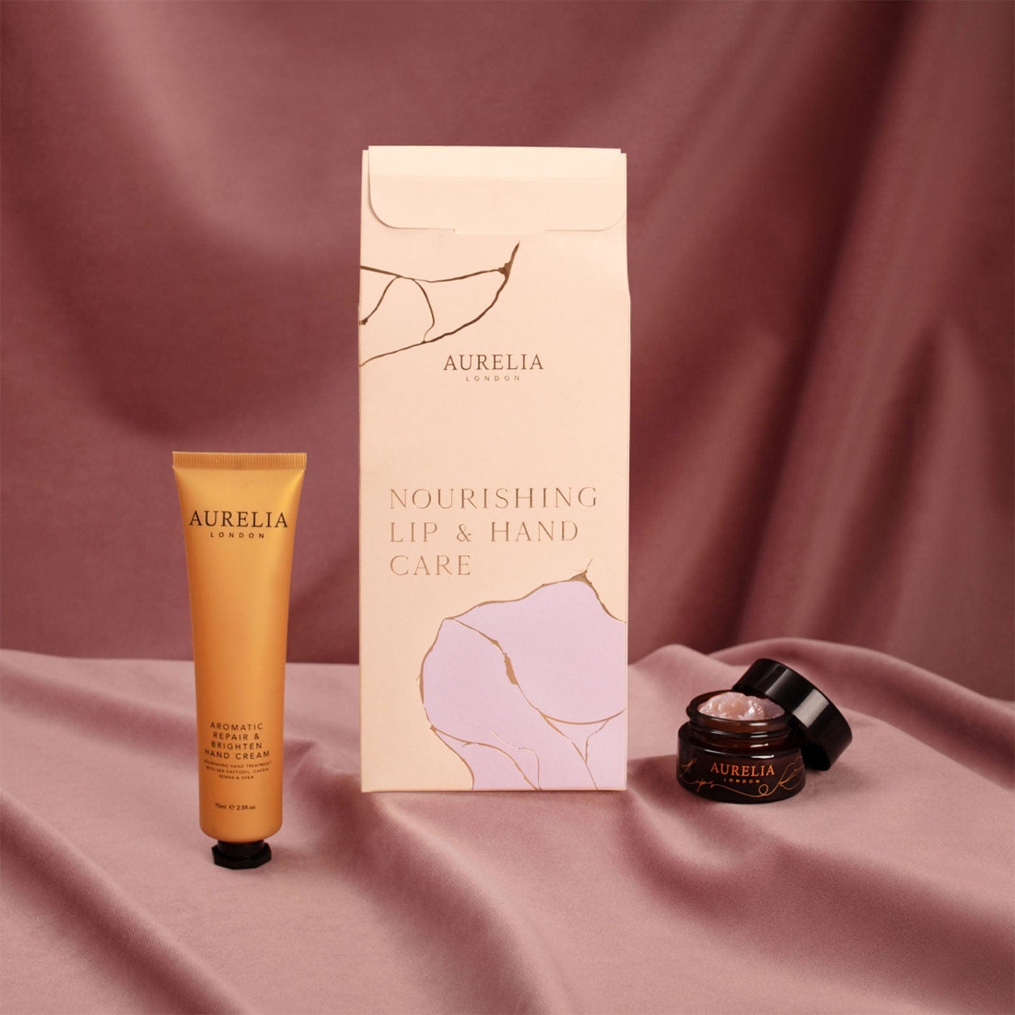 Aurelia lip and hand care products on a pink fabric background