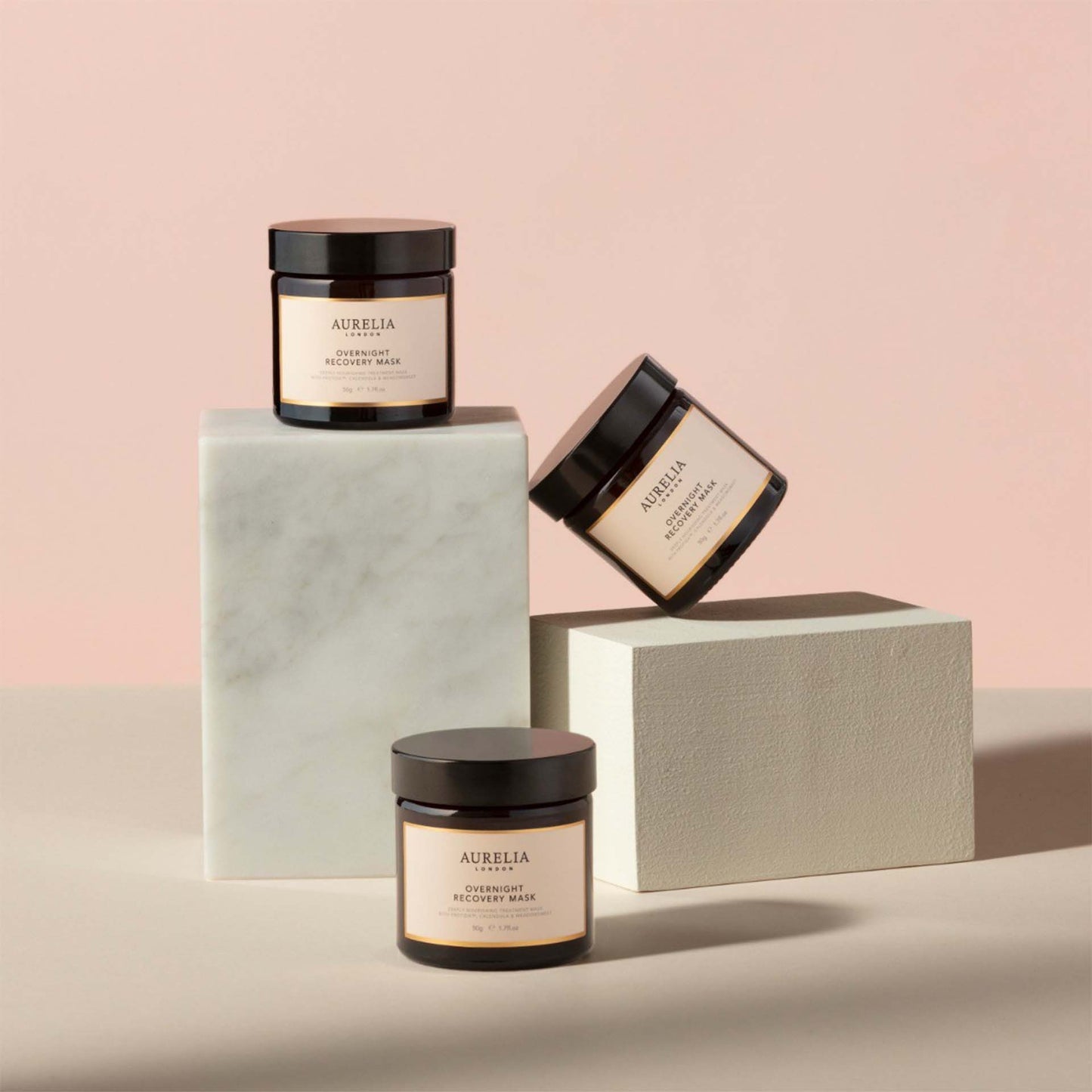 Three jars of Aurelia overnight recovery mask on a light pink background