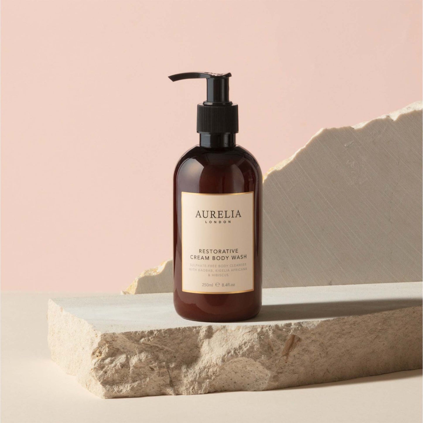 Aurelia London body wash bottle on a stone surface with a pink background