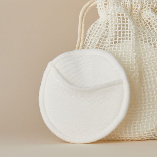 Round white reusable bamboo cotton pad on a beige background with a mesh bag.