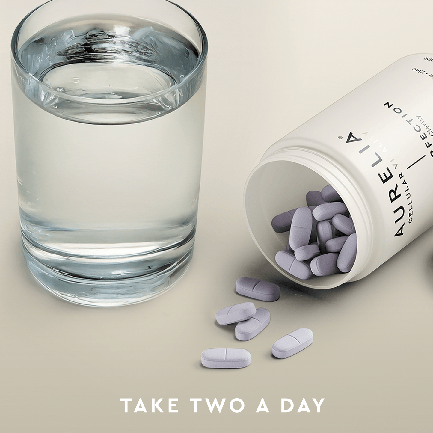 Glass of water next to an open bottle of Aurelia supplements with scattered pills on a light background.