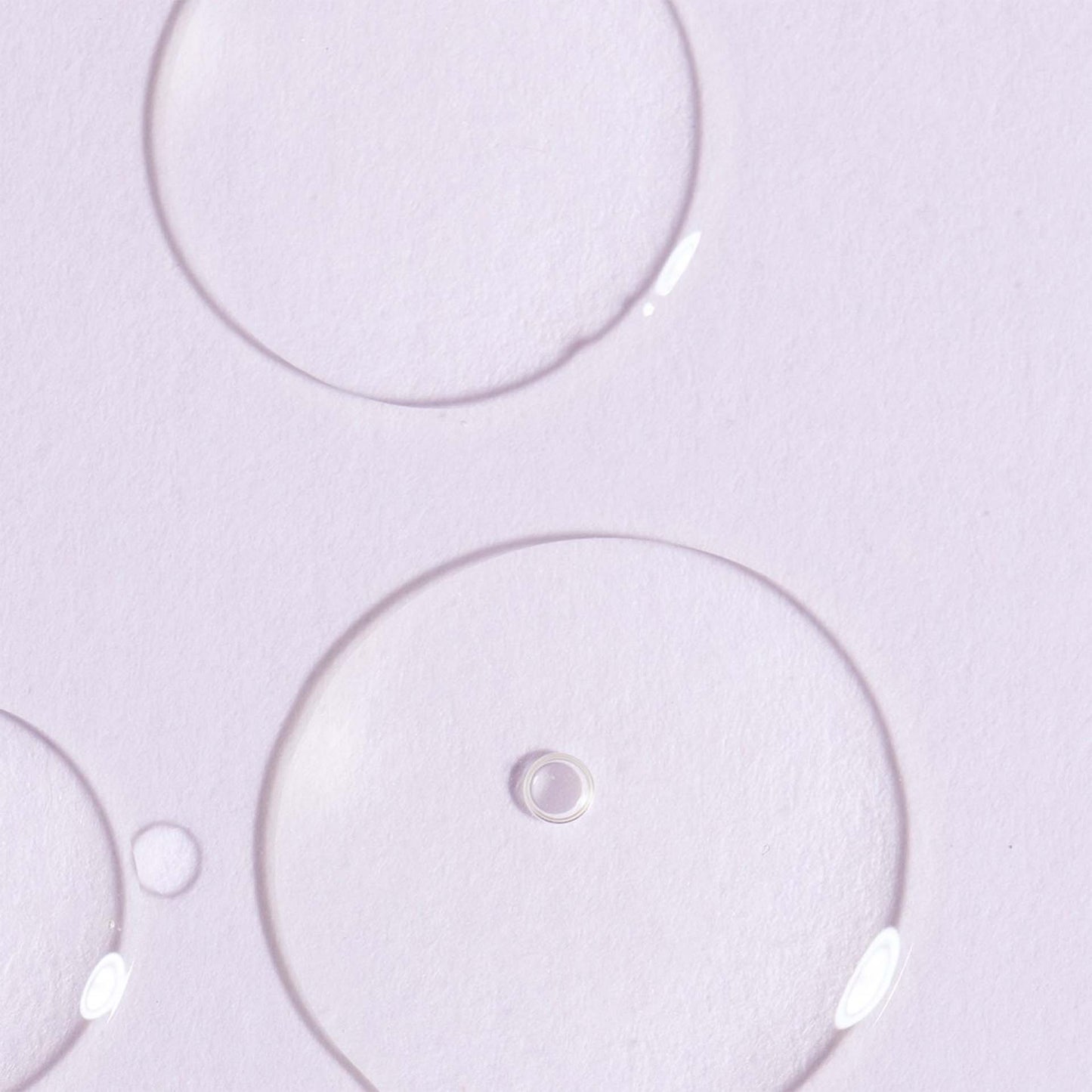 Close-up of clear massage oil bubbles on a light purple background
