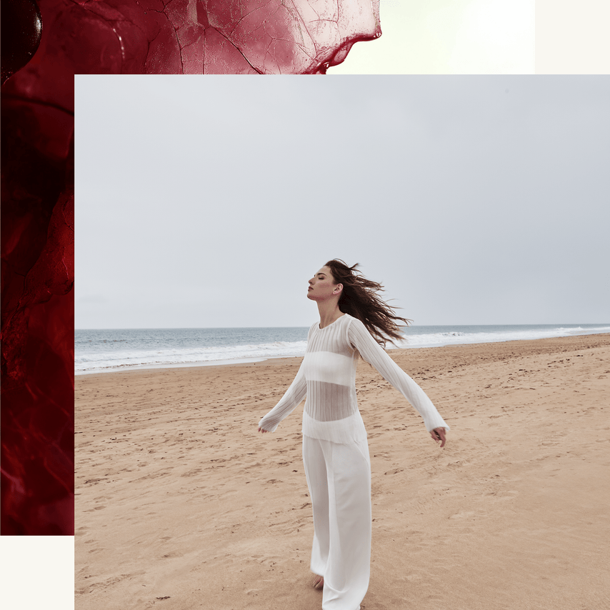 Woman in a white outfit standing on a beach with a red textured object in the corner.