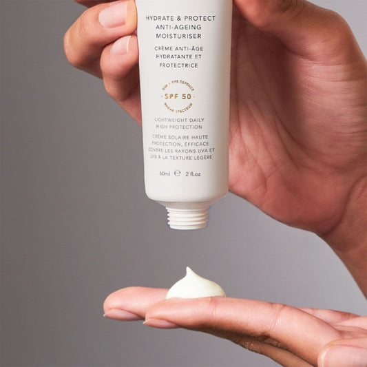 Hand holding a skincare product with visible cream on the palm against a gray background