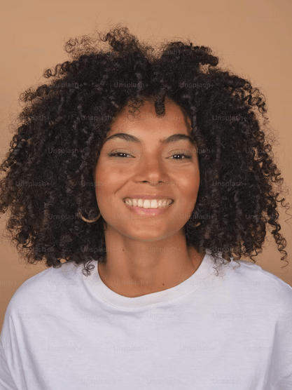 Woman with curly hair wearing a white shirt against a beige background